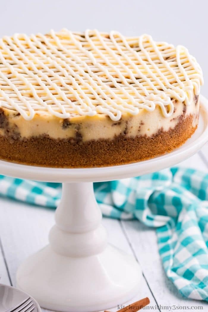 The whole cinnamon roll cheesecake on a standing platter.