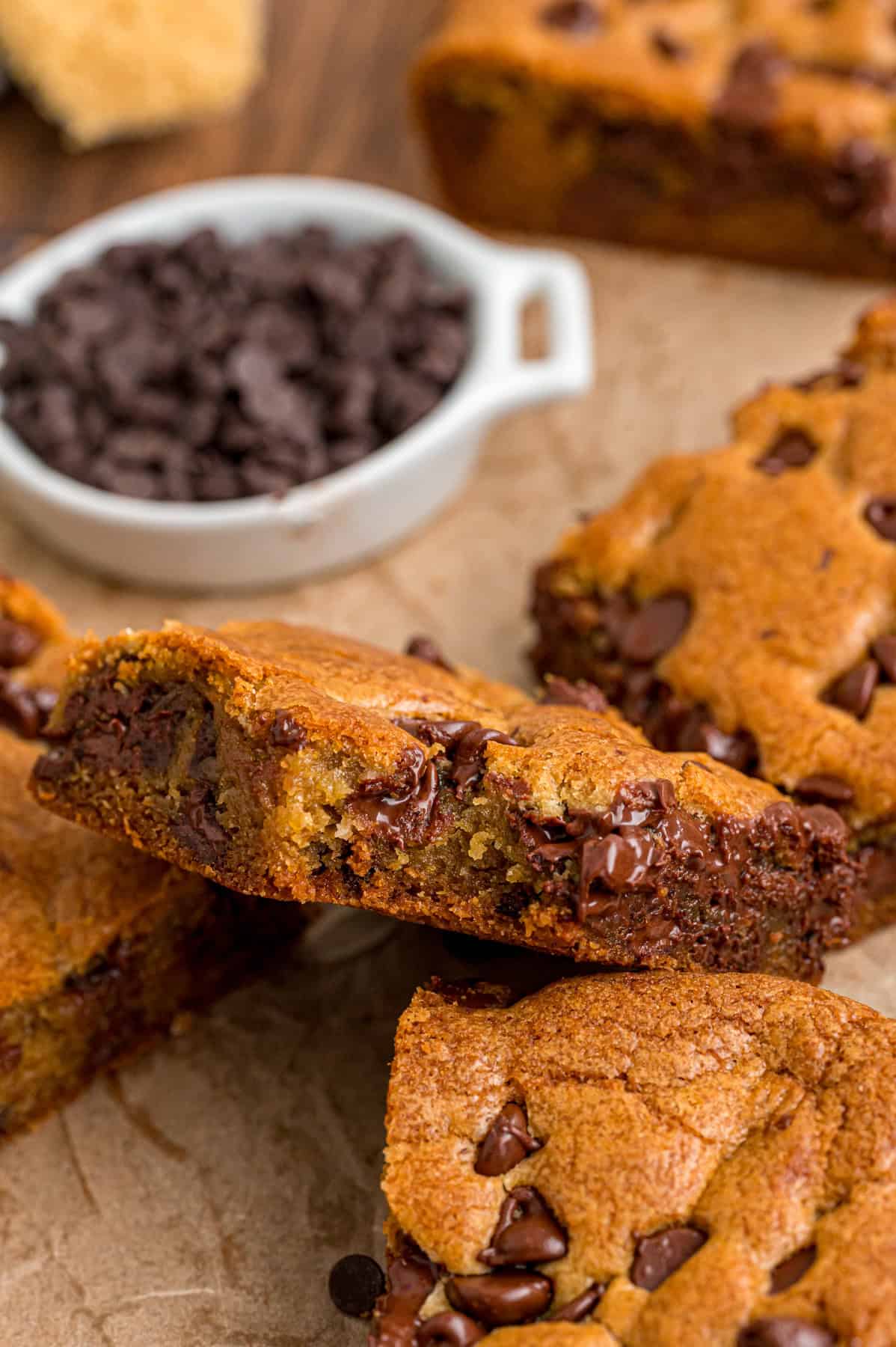 Chocolate chip cookie bars on parchment paper, one on its side to show the chocolate inside