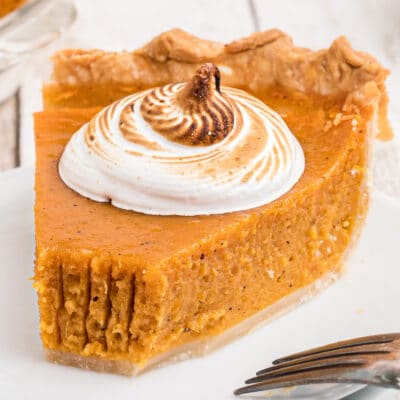 A close-up of a single slice of Sweet Potato Pie topped with whipped cream and with a bite taken out of it.