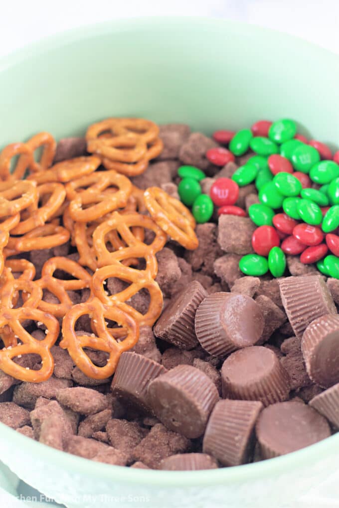brownie batter Chex, pretzels, Christmas M&M'S, and Reese's Peanut Butter cups in a large mint green mixing bowl.