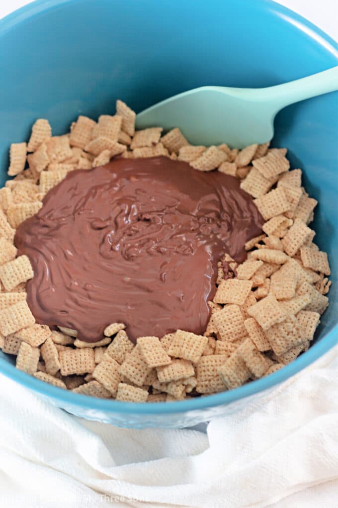 large blue mixing bowl filled with Chex and melted chocolate.