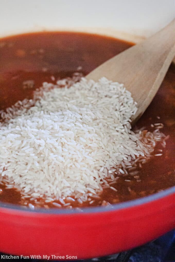 adding white rice to the tomato and broth mixture in a large pot.