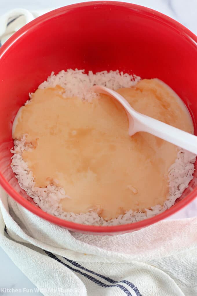 stirring coconut, vanilla, and sweetened condensed milk together in a red bowl.