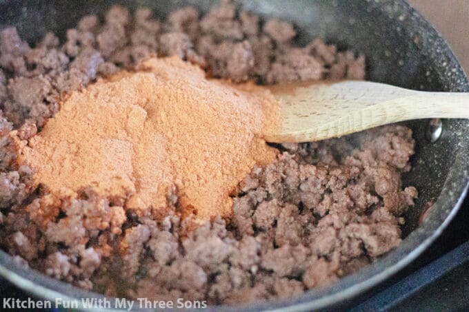 adding taco seasoning to the ground beef in the pan.