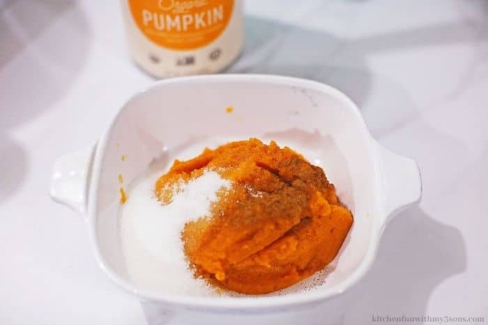 Sugar being added to pumpkin puree in a bowl.