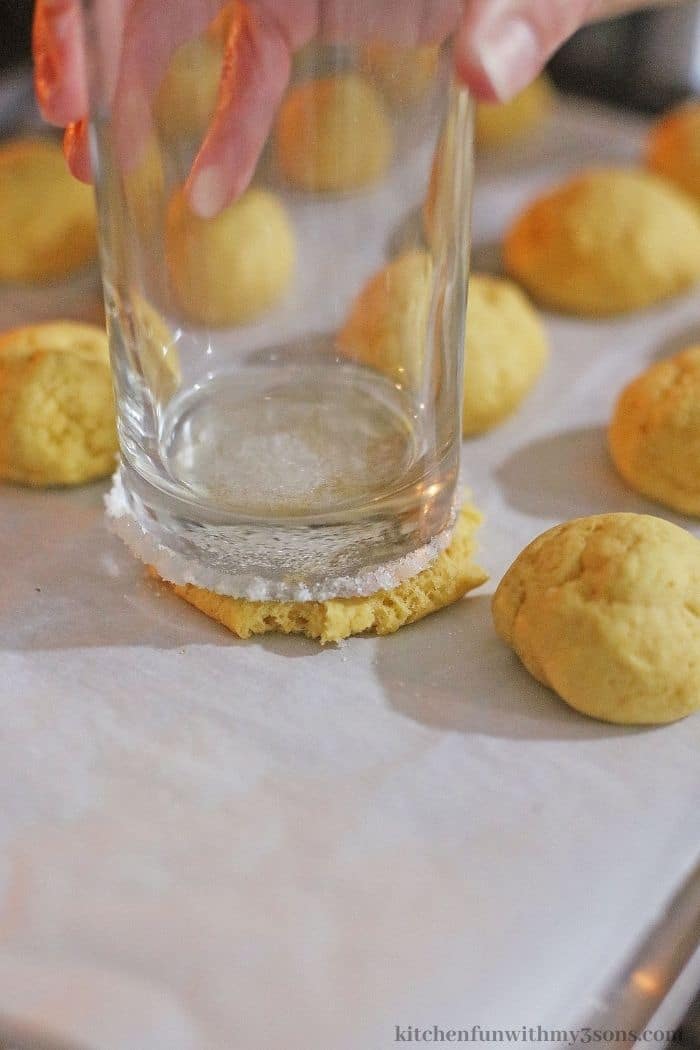 Cookie dough balls being pressed down with the bottom of a glass..