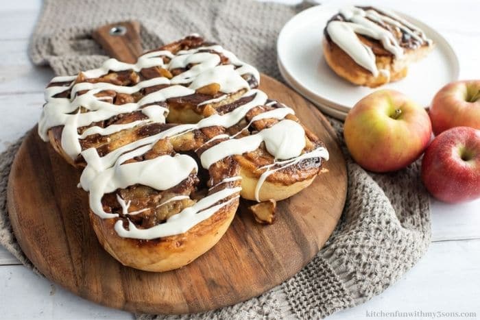 The apple cinnamon buns on top of a wooden board.