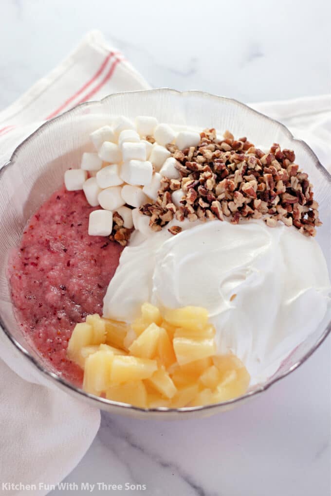 Cool whip, pecans, pineapple chunks, mini marshmallows, and crushed cranberries in a bowl.