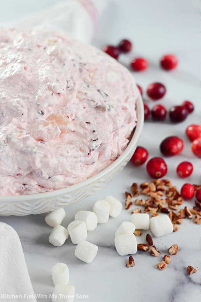 Cranberry Fluff Salad in a bowl surrounded by marshmallows, fresh cranberries, and pecans.