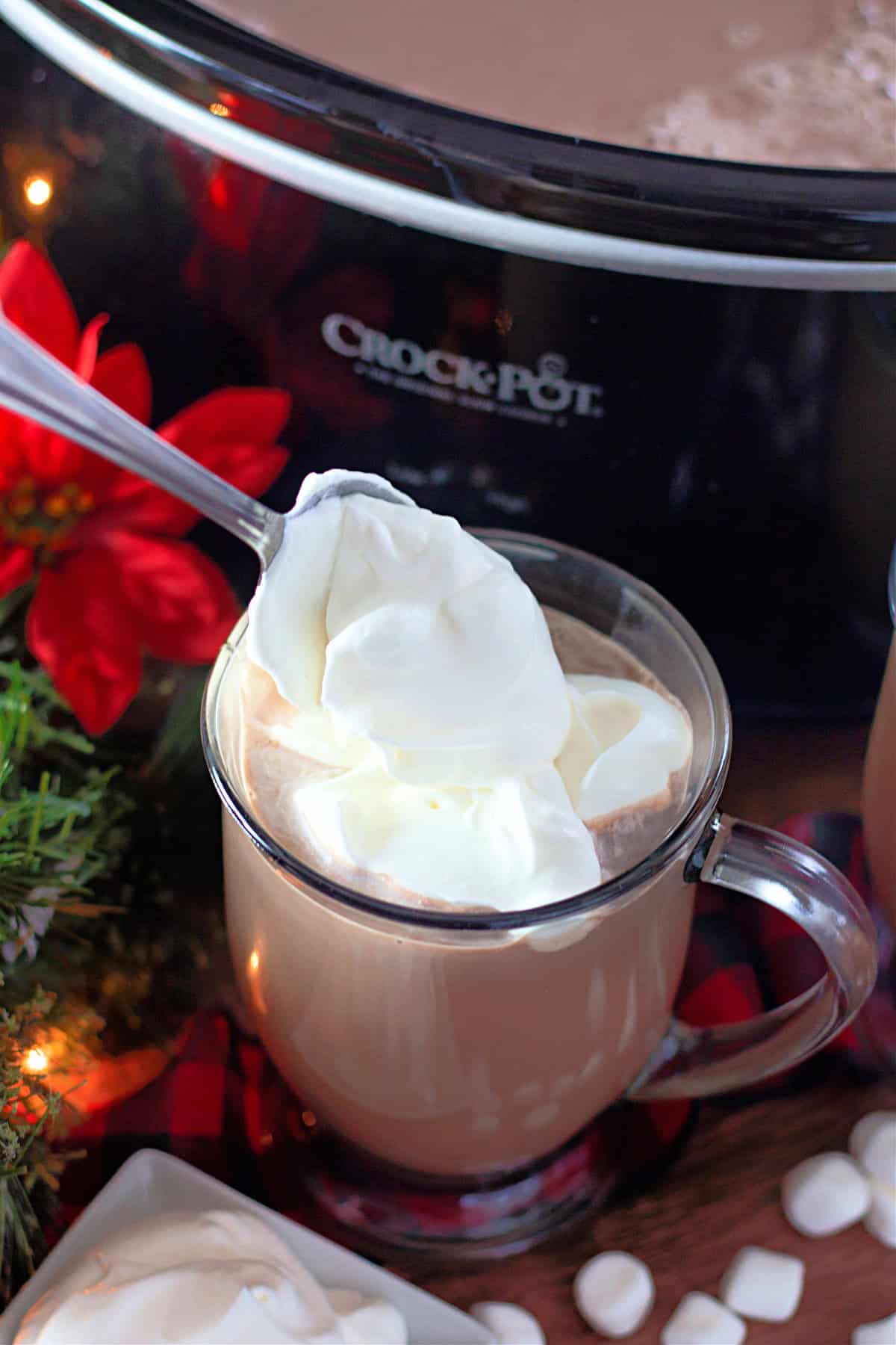 Adding whipped cream to a mug of slow cooker hot chocolate