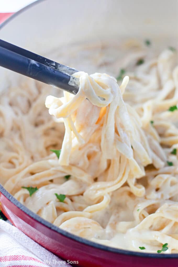 lifting up tongs filled with fettuccine alfredo.