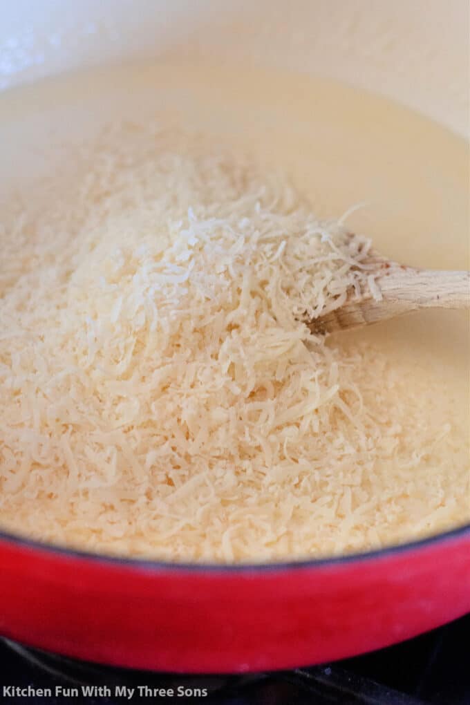 adding freshly grated parmesan and romano cheeses in a red pot with a wooden spoon.
