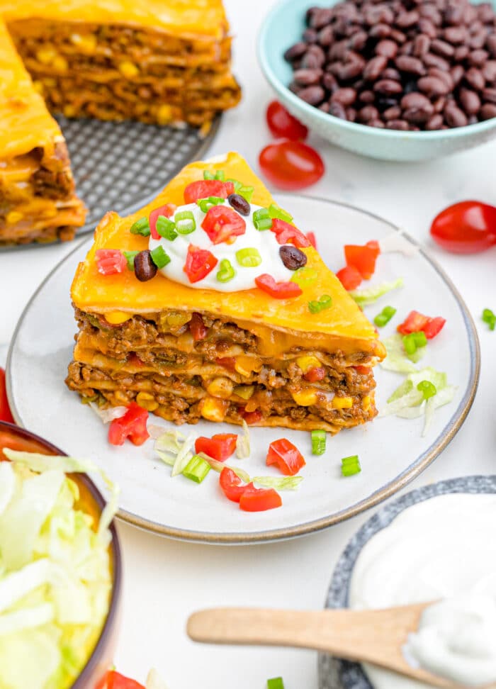 A slice of baked taco pie on a plate, topped with sour cream and chopped veggies.