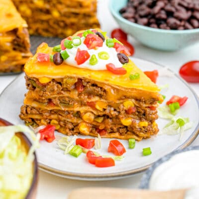 A slice of baked taco pie on aplate, topped with sour cream and chopped veggies.