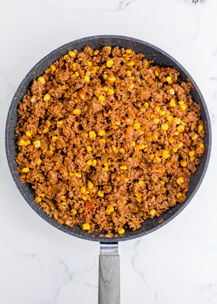 A skillet on a white background with taco meat and corn inside.