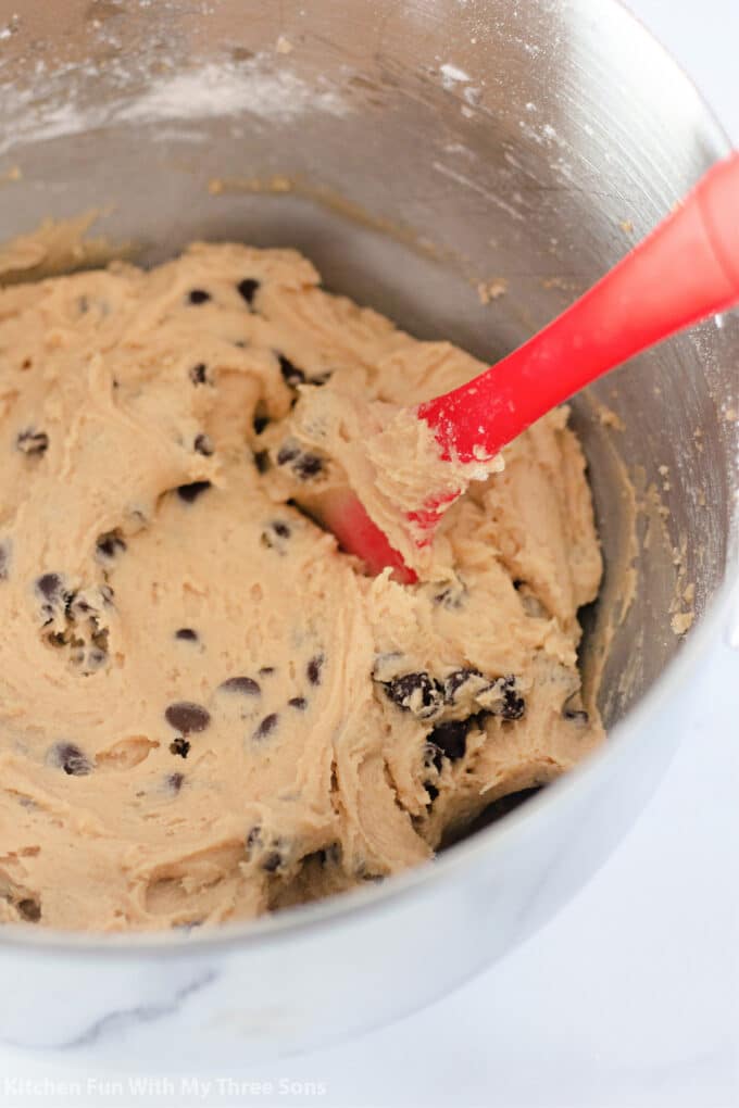chocolate chip cookie dough in a metal mixing bowl with a red spatula.