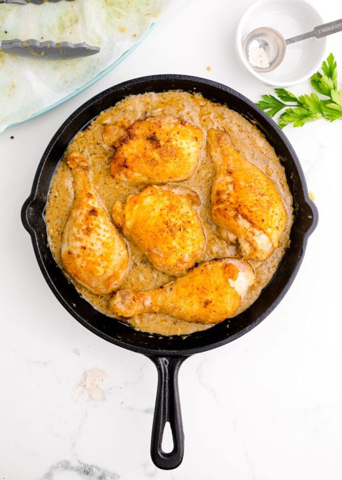 Fried chicken pieces in gravy in a cast-iron skillet on a white background.