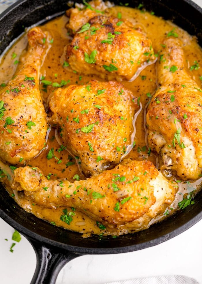 Close-up shot of smothered chicken, garnished with parsley, in a skillet.