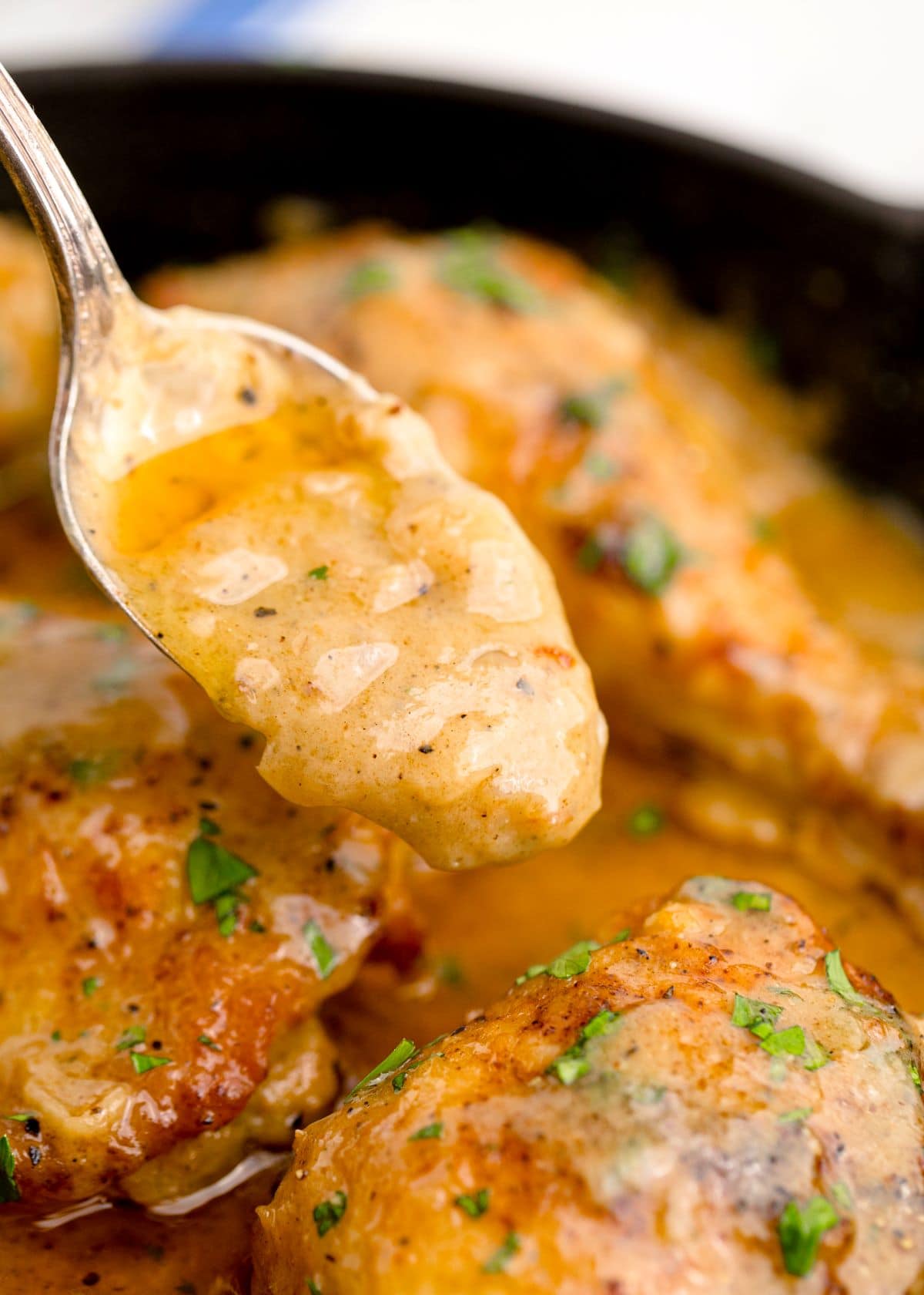 Close up shot of three chicken pieces with gravy. A spoon is lifting some of the gravy out of the pan.