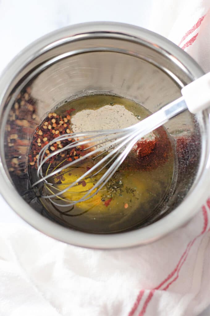oil and spices in a metal mixing bowl with a whisk.