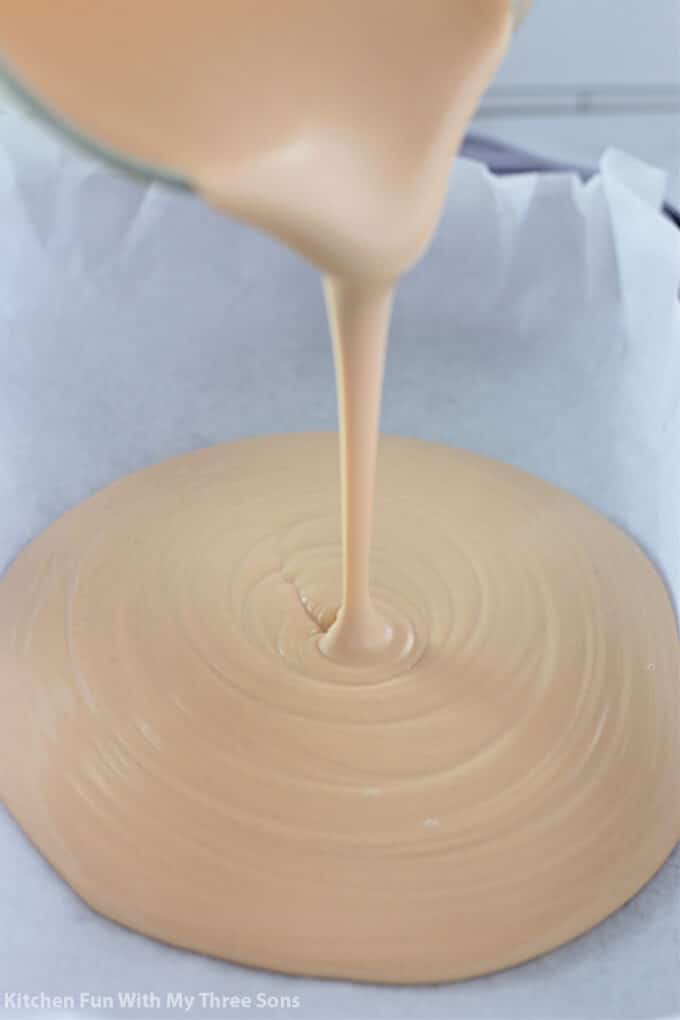 pouring the mixture of white chocolate and peanut butter into a prepared dish.