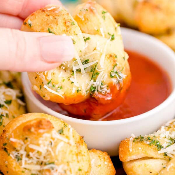 A homemade garlic knot is dipped into marinara sauce.
