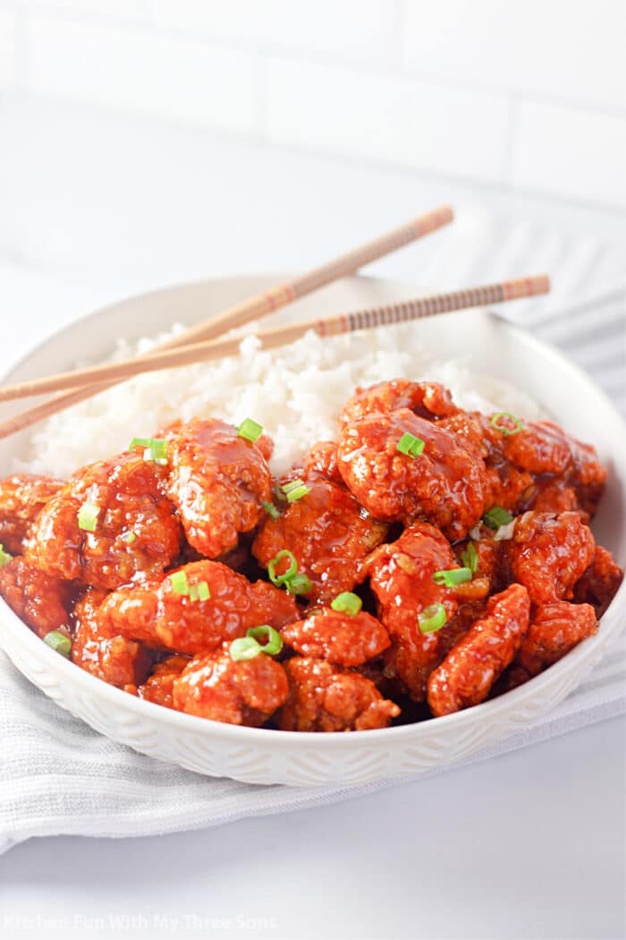 4 Ingredient Orange Chicken in a white bowl with rice and chopsticks.