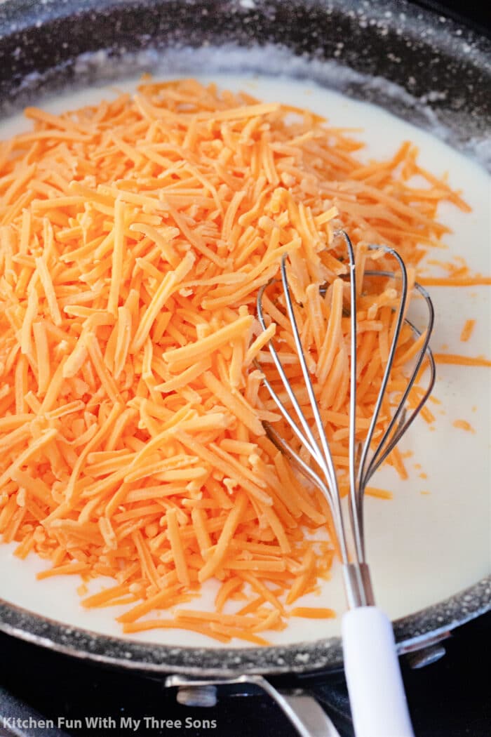 adding grated cheddar cheese to the skillet with a whisk.