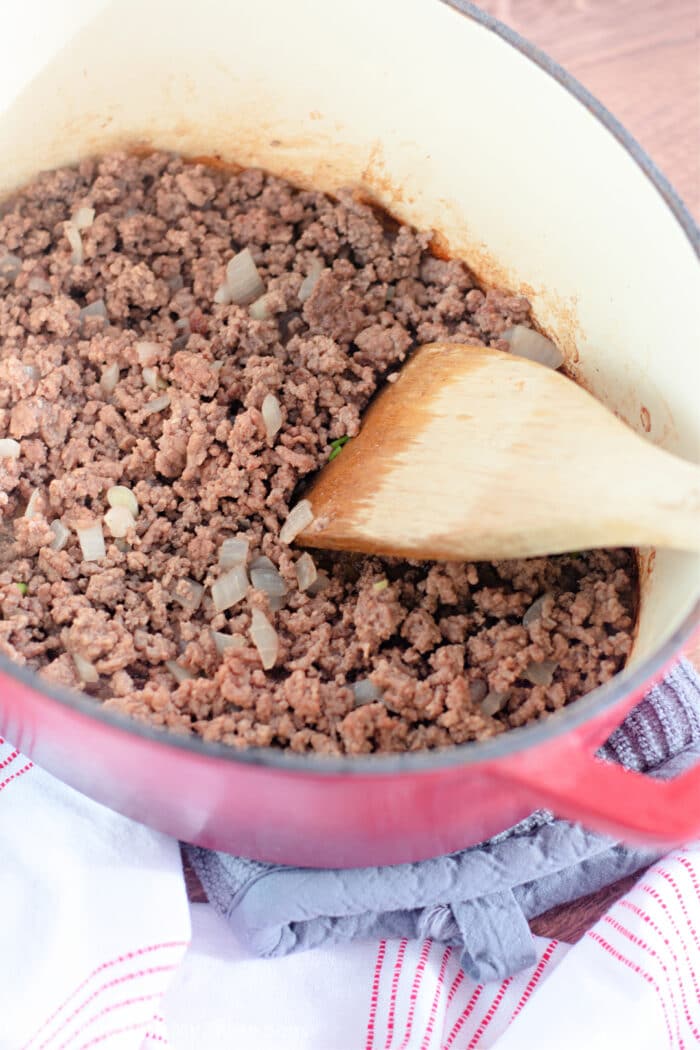 cooking ground beef and onions in a large pot with a wooden spoon.