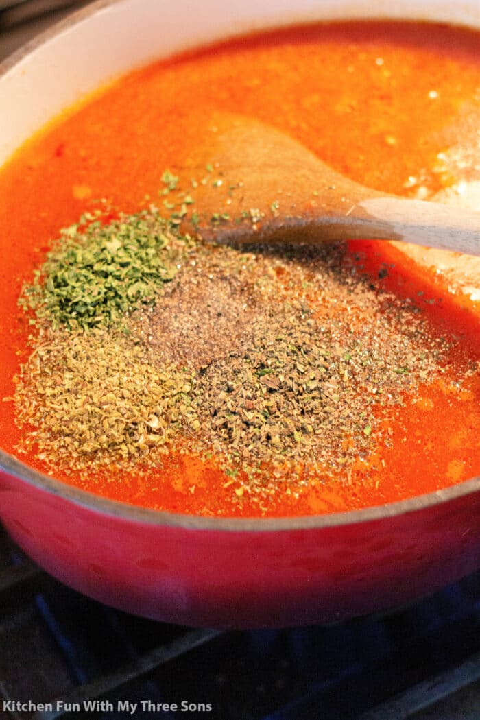 herbs and spices in a pot of tomato soup base.