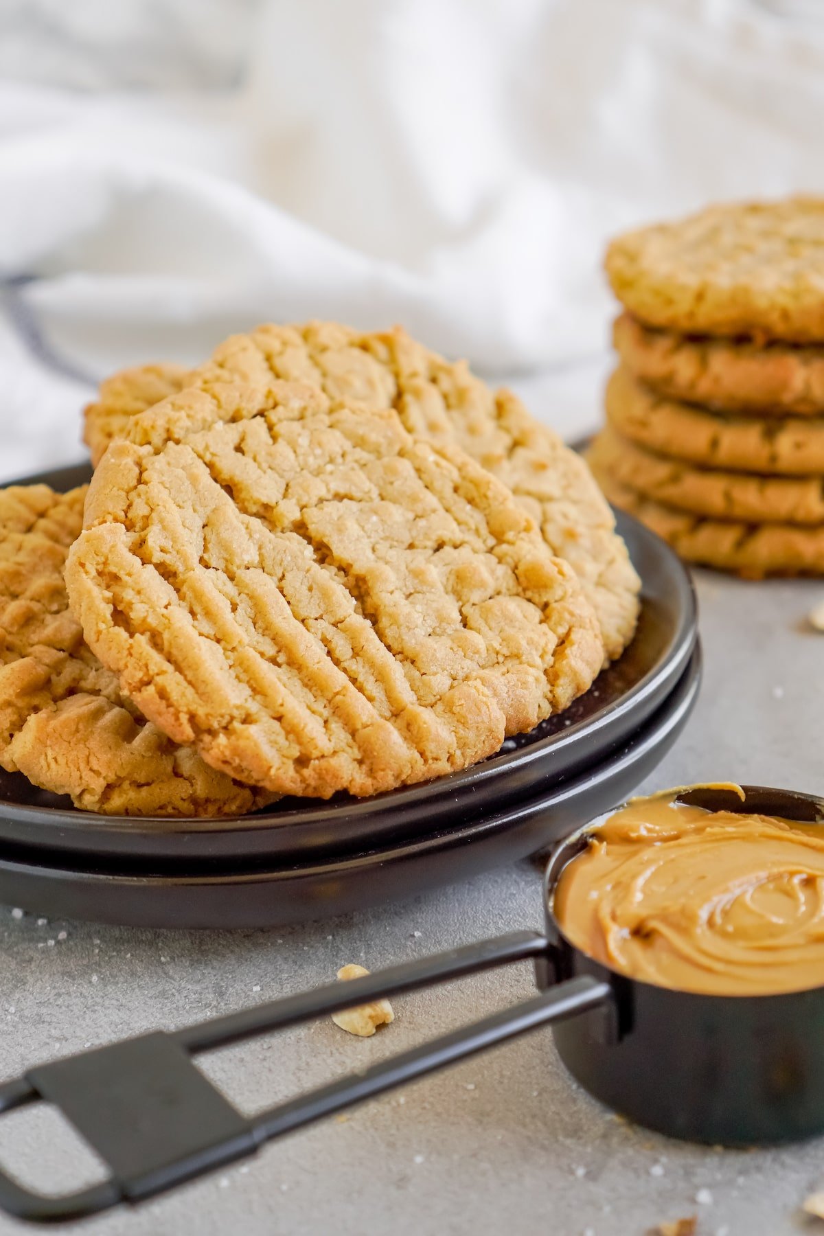 A plate of peanut butter cookies next to a measuring cup full of peanut butter.