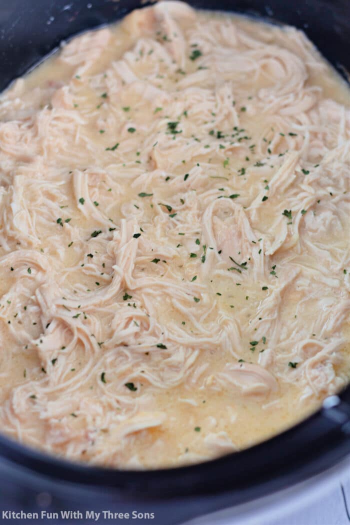 creamy chicken in a slow cooker topped with parsley.