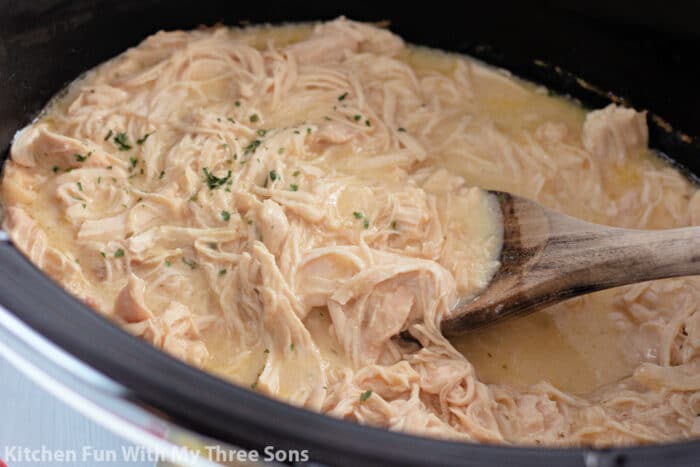 shredded chicken in a slow cooker with a wooden spoon.