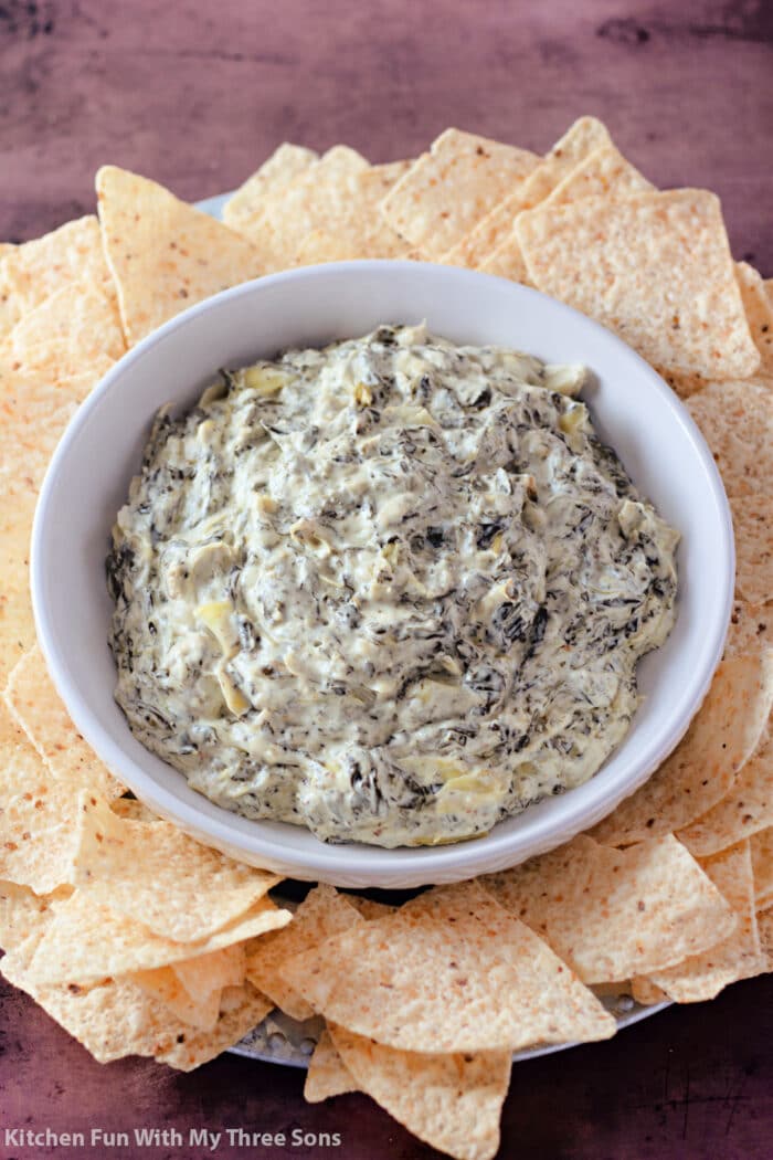 A tray of tortilla chips with a bowl of spinach artichoke dip in the center.