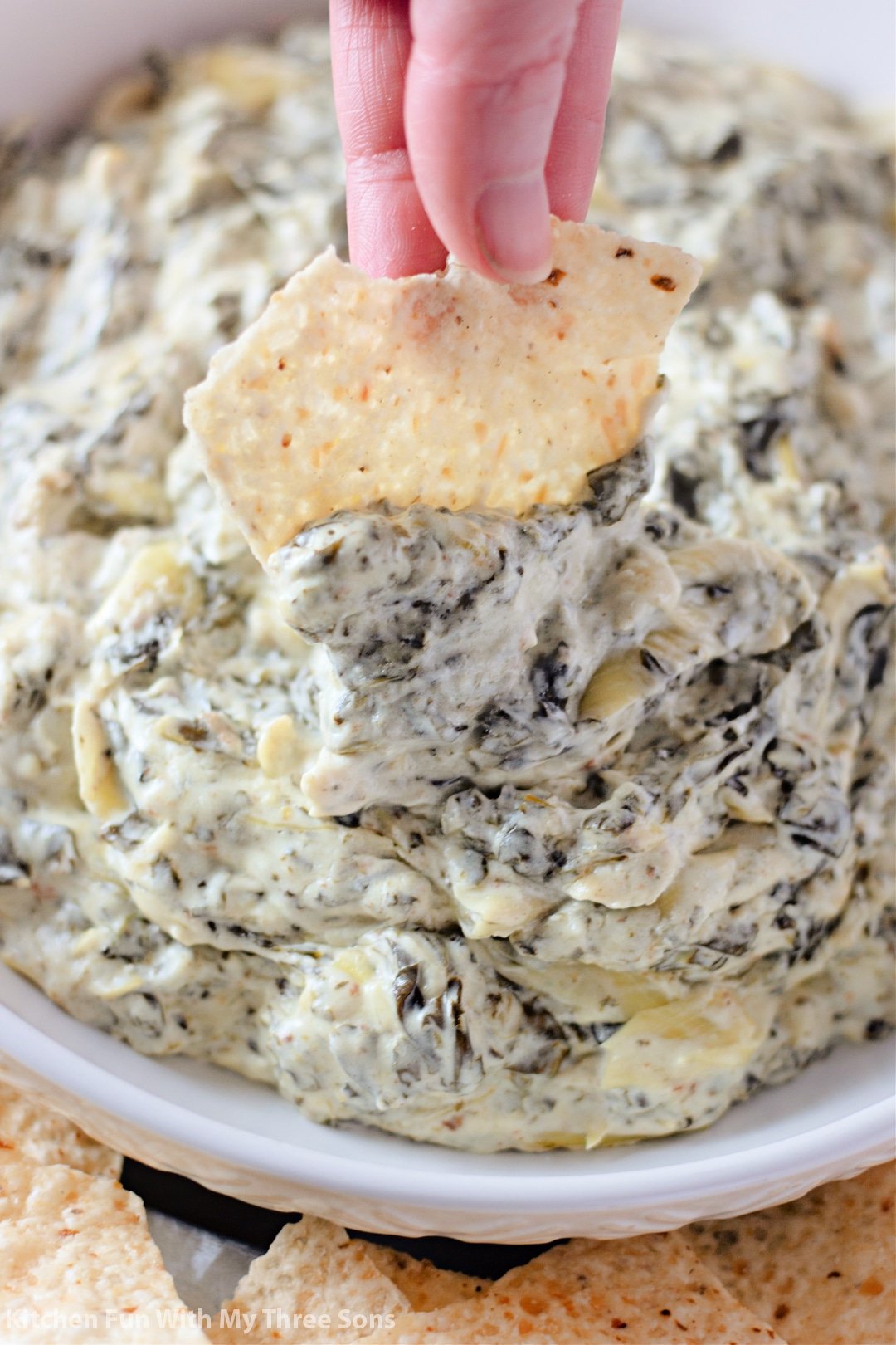 Dipping a tortilla chip into spinach artichoke dip.