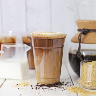 A cup of brown sugar oat milk shaken espresso on a table with other ingredients.