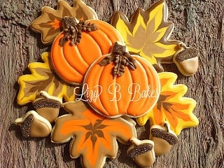 A pile of sugar cookies on top of a wooden surface with frosting designs of pumpkins, acorns and leaves