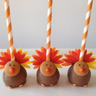 Three turkey cake pops with orange and yellow sticks stuck into them