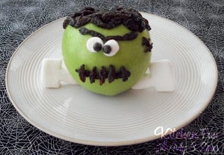 An apple decorated to look like Frankenstein with edible googly eyes