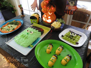 A bunch of Frankenstein-themed party food on a table with a light-up pumpkin Halloween decoration