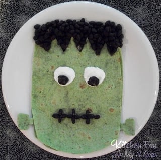 A green tortilla decorated with edible eyes, hair and a creepy stitched mouth