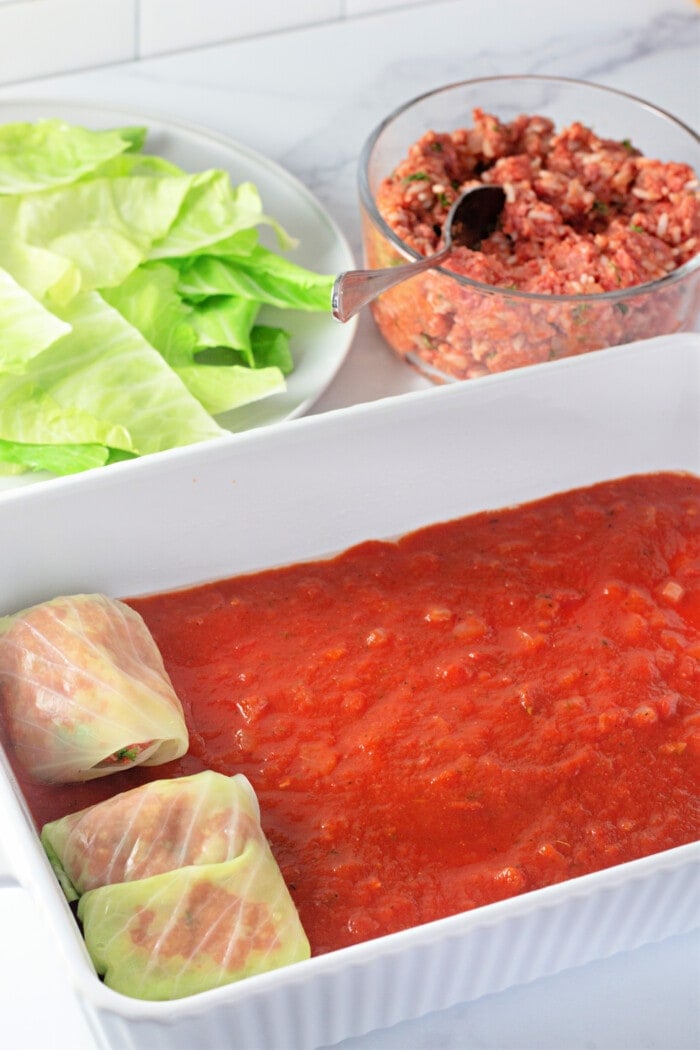 adding cabbage rolls to a pan over the sauce