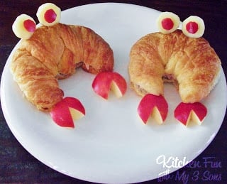Two croissant sandwiches decorated to look like crabs on top of a plate