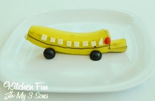 A banana carved and decorated to look like a school bus on top of a white snack plate