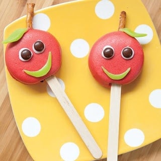 Two apple candy pops with smiley faces on top of a polka-dotted plate