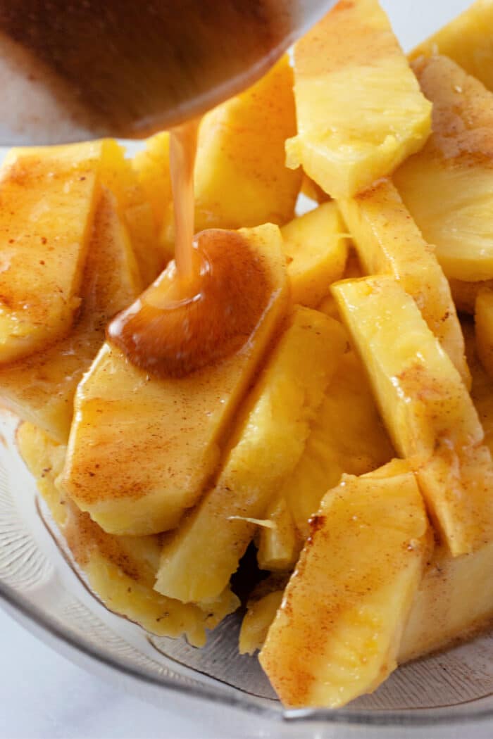 pouring melted butter, maple syrup, and cinnamon over fresh pineapple slices.