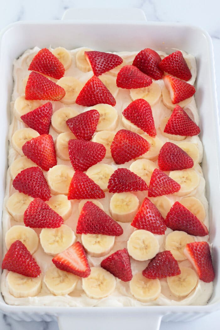 Strawberries and bananas layered on top of pudding in a pan