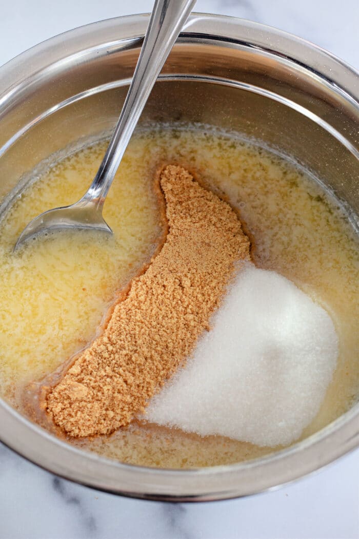 mixing crushed graham crackers, butter, and sugar together in a metal mixing bowl.