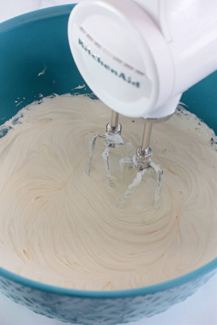 beating cream cheese, powdered sugar, and Cool Whip together in a teal mixing bowl with an electric mixer.