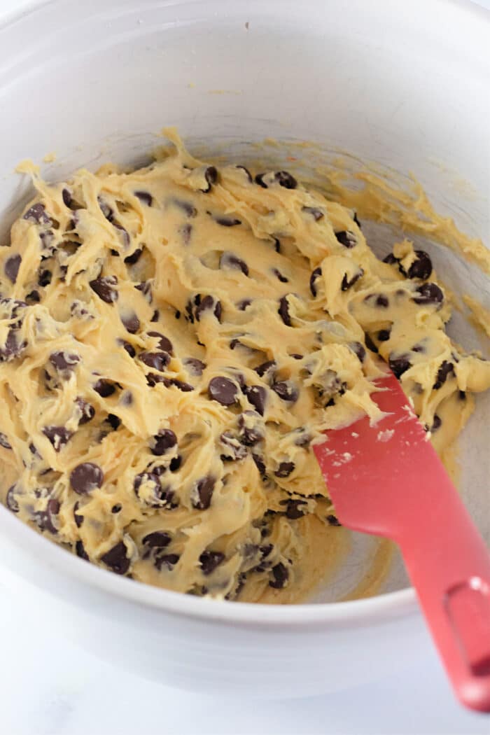mixing the cookie batter in a white bowl with a red spatula.